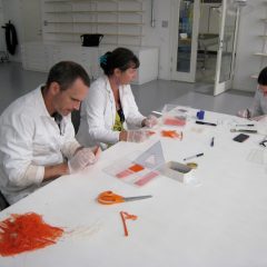 Tre personer sitter i vita laboratorierockar runt ett bord och pillar med textilfibrer för testerna.