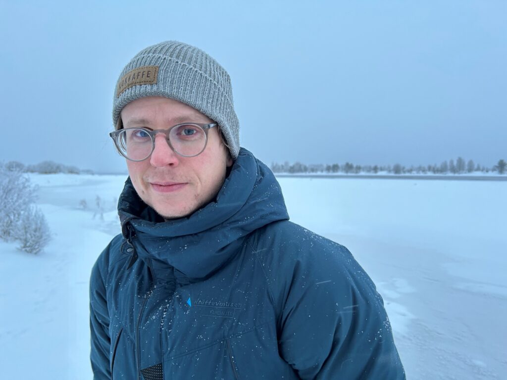 Man med mössa på stranden till en frusen älv.