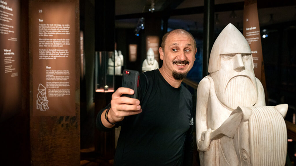 En man tar en selfie bredvid en skulptur föreställande en viking.