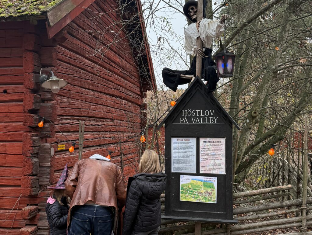 Vuxen man och två barn tittar på en skylt på ett friluftsmuseum