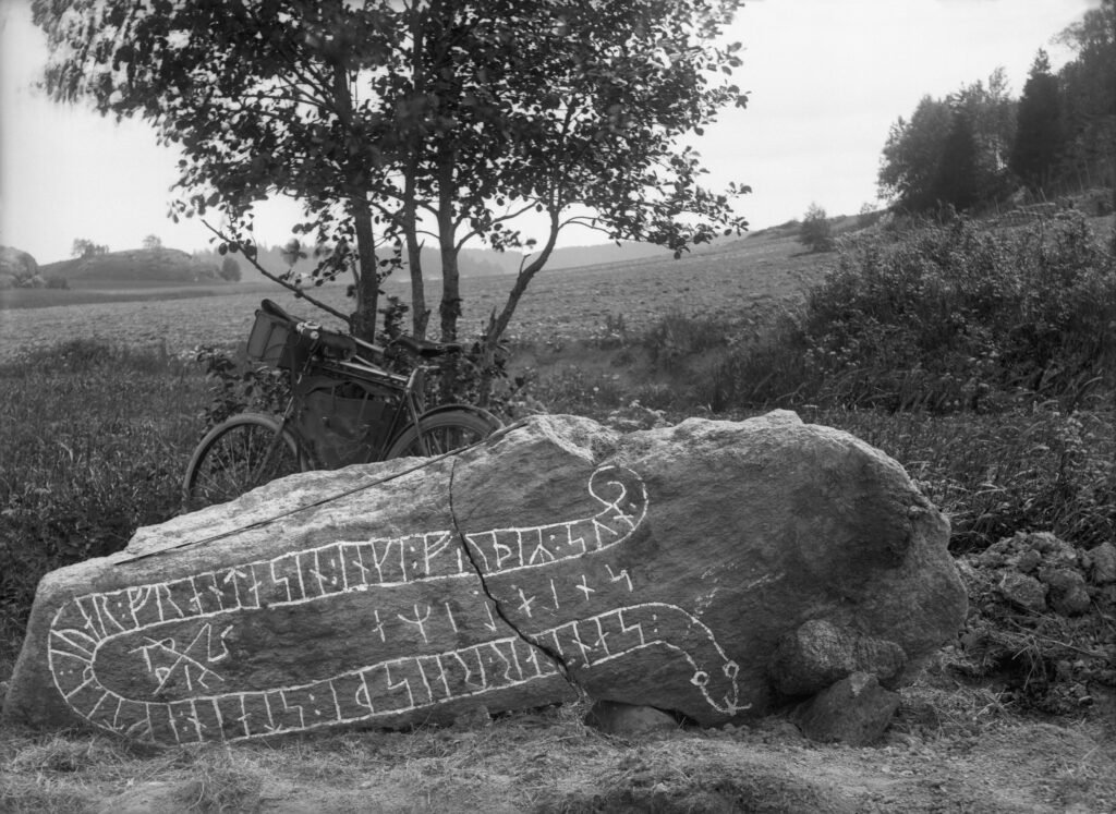 Svartvitt fotografi av liggande runsten framför cykel.