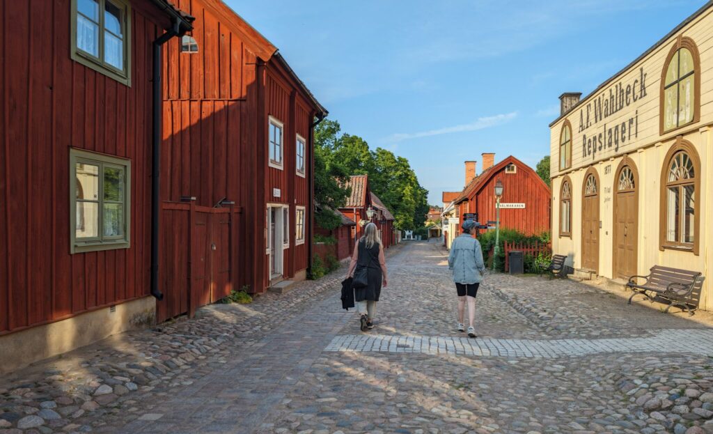 Två damer vandrar i gamla kvarter på en bred kullerstensgata omgiven av gamla träbyggnader.