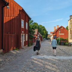 Två damer vandrar i gamla kvarter på en bred kullerstensgata omgiven av gamla träbyggnader.