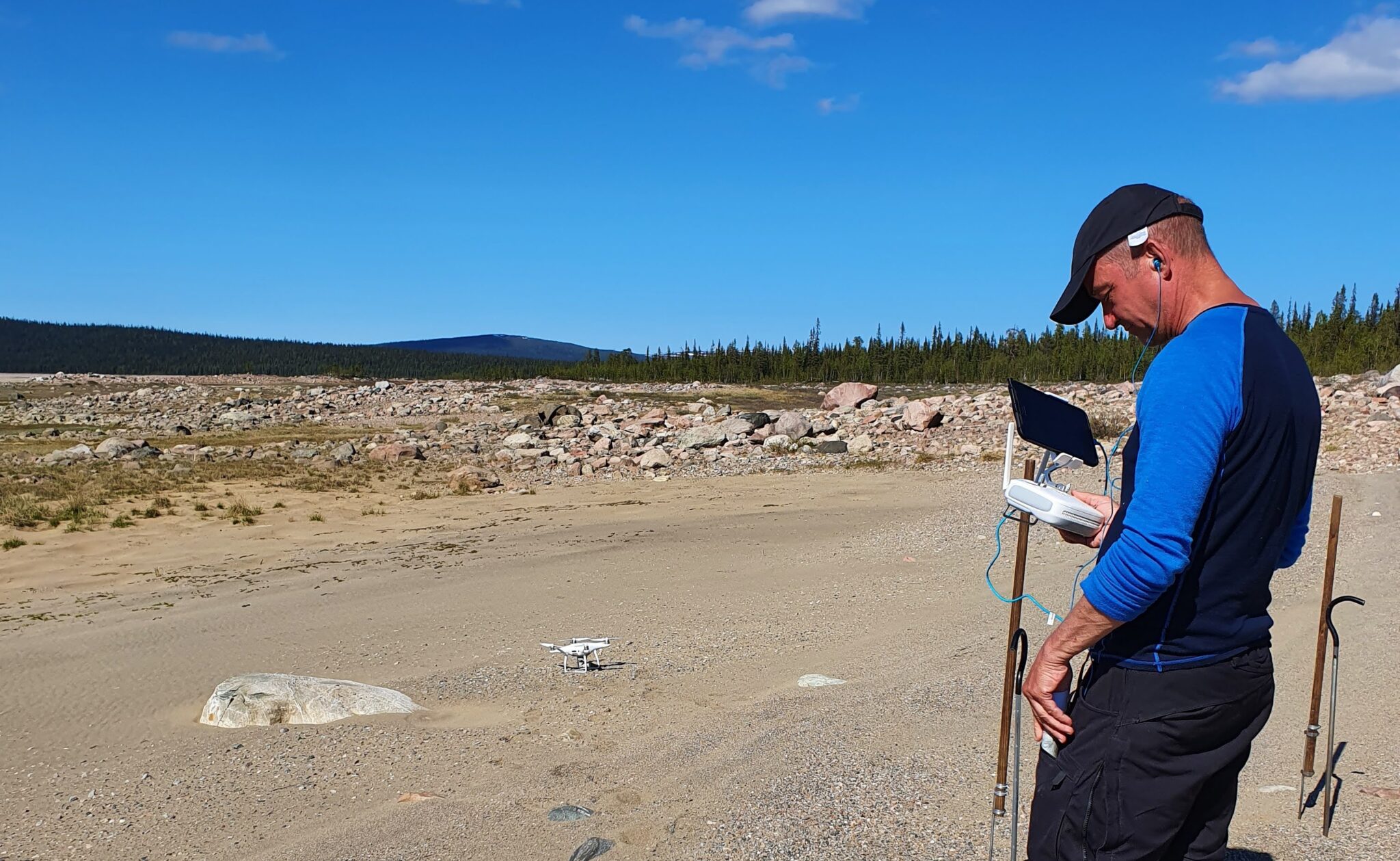 Man står med keps i ett fjälllandskap och manövrerar en drönare