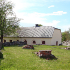 En kulturmiljö med stenmurar och en byggnad. I marken närmast rester efter ett tidigare kloster.